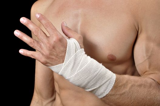 Closeup of shirtless male athlete with injured wrist bandaged in sports wrap on black background