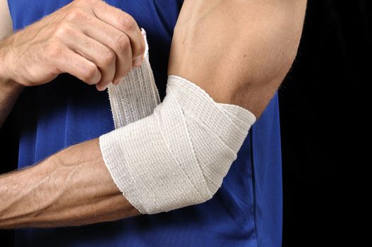 Closeup of athletic man tending injured elbow with sports wrap on black background