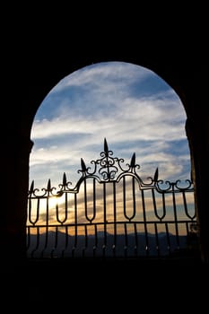 The sun sets over the Spanish mountains through an old stone arch in Ronda.