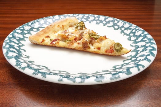 Single piece of pizza with many toppings lying on a plate