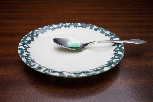 Pill resting on a spoon that is on a dinner plate.