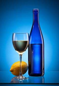 blue bottle with white wine and full glass with lemon over blue