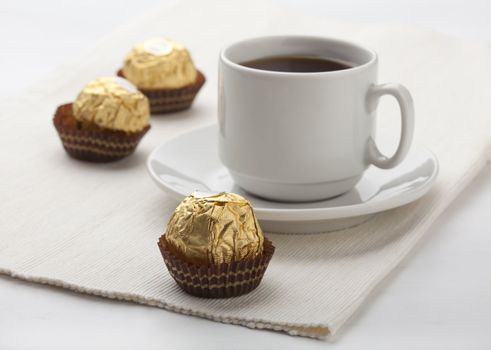 Three candies in golden cover with cup of coffee on the napkin