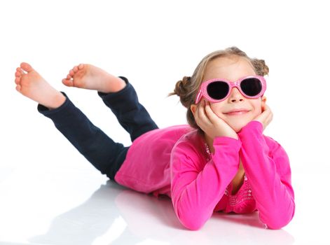 Little fashion girl lying in pink dress and sunglasses. Isolated white backround.