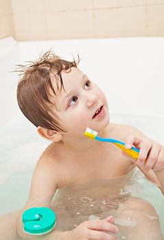 Cute little boy sitting in the full bath and holding toothbrush