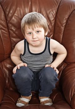 Portrait of cute blond little boy sitting in a leather armchair