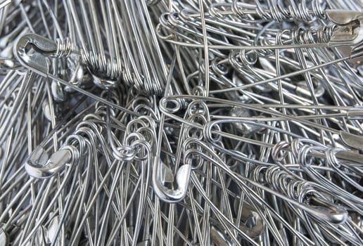 Silver colored big safety pins pile closeup as background