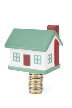 Little house toy on a stack of coins isolated over white background