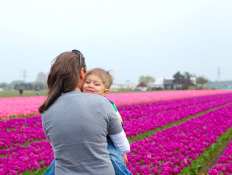 Little boy and his mother with bouquet between of the yellow-red tulips field