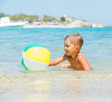 Portrait of little boy swimming and plaing with ball in the transparent sea