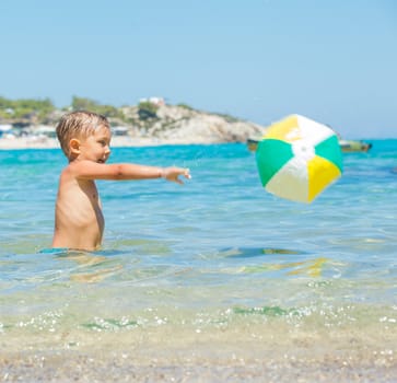 Portrait of little boy swimming and plaing with ball in the transparent sea