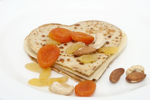 heart-shaped pancake with dried apricots, almond, hazelnuts, cashew and raisins on white plate