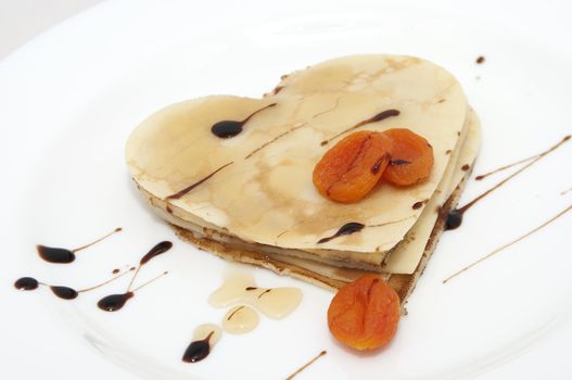 heart-shaped pancake with dried apricots and honey on white plate