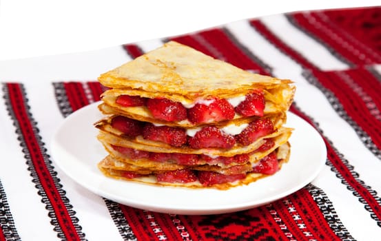 Pancakes with custard cream and strawberries on traditional ukrainian towel