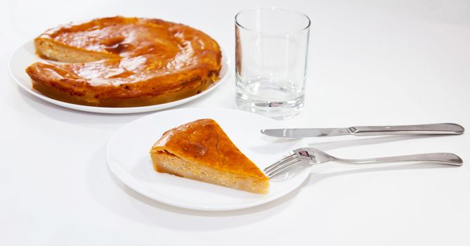 Piece of onion pie with fork and knife and glass on white background