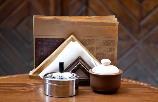 Sugar-bowl, napkin, newspaper and ash tray on the wooden table