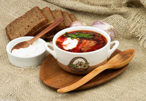 Borscht. Traditional Soup with Beet, Vegetables, Meat Arranged with Brown Bread, Garlic and Sour Cream on Wooden Plate with Wooden Spoon