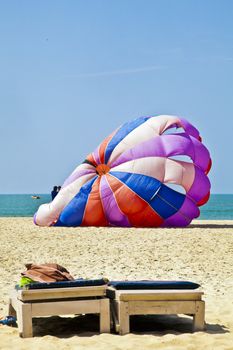 Vertical seaside coastal ocean landscape, beach towels, slippers and quest stools from a typical and generic tropical beach scene of para gliders about to take flight over the ocean and beach area of Goa India