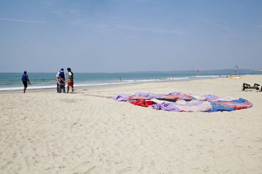 Workers getting a customer ready for paragliding over the sandy shoreline on a secluded beach patrolled by lifeguards