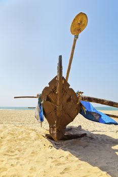 Vertical portrait of abstract fishermans catamaran with an oar / paddle on a sandy beach and under blue skies. Generic shot of the east, this location is in Goa, India