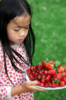 child holding a plate of cherry and strawberries on green background