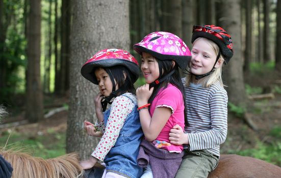 three friends:  one caucasian blond and two  asian (9 years +5 years) on horses in a forest