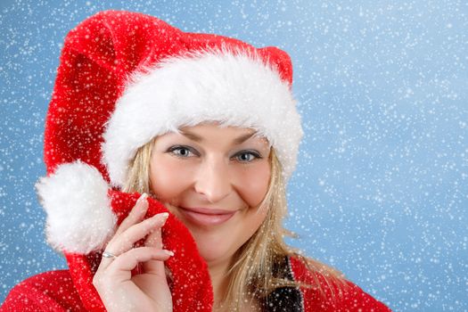 Joyful pretty woman in red santa claus hat smiling on blue background