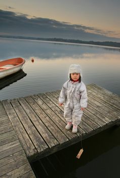 Chinese child with hat in winter looking at the camera
The child stands in front of a lake and hold a small wooden boat
 