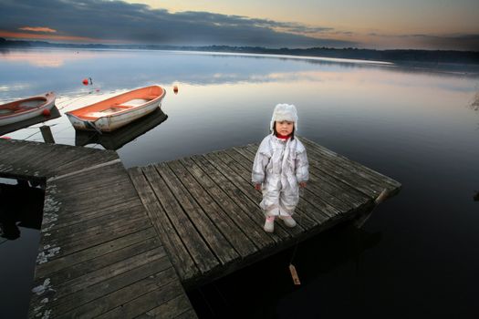 Chinese child with hat in winter looking at the camera
The child stands in front of a lake and hold a small wooden boat
 