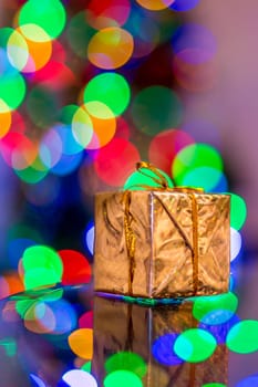 Glittering Christmas gift wrapped in gold foil with Christmas light bokeh in the background