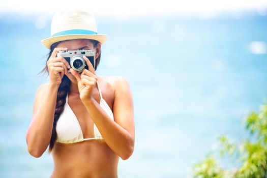 Summer beach woman holding vintage retro camera taking pictures looking at camera during summer holiday vacation travel at the ocean.