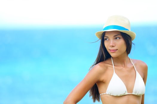 Woman beach portrait looking to side with wearing hat and beachwear bikini. Beautiful young modern multiracial female model looking serious with subtle smile. Half asian and half caucasian model outdoors.