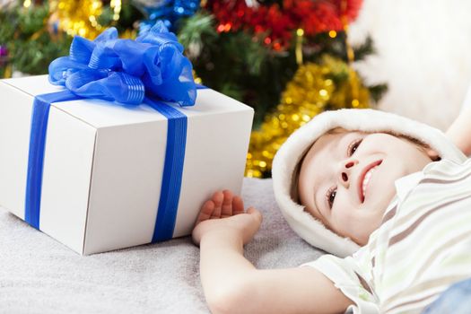 Cute smiling child boy in Santa Claus hat with new year present or christmas holiday gift box