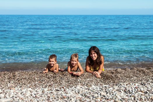 Summer vacations - happy mother with two little smiling child boy brothers playing on blue sea sand beach