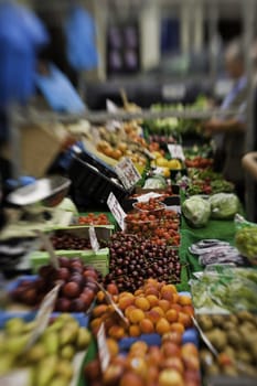 Colourful view down the counter of a stall laden with a variety of fresh fruit and vegetables at a farmers market with selective focus to cherries