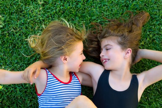 Blond and brunette sisters kid girls smiling lying on garden grass