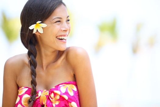 Beach woman happy looking to side laughing having fun smiling joyful and elated wearing sarong and flower on Hawaii. Multiracial Asian / Caucasian girl.