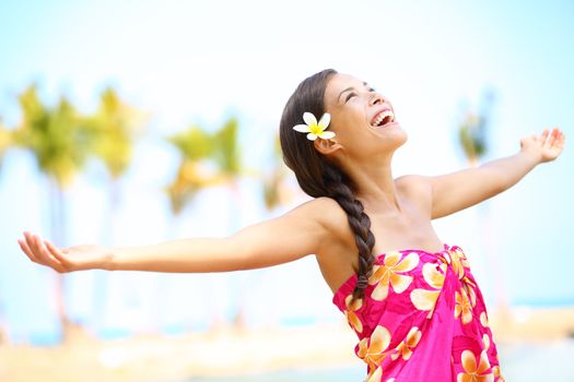 Free happy elated beach woman in freedom joy concept. Beautiful girl smiling with arms out looking up joyful on Hawaiian beach. Mixed race Asian / Caucasian girl.
