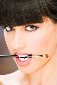 pretty woman hold make up brush between teeth