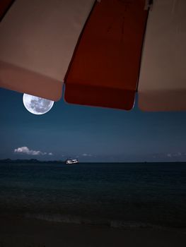Sunshade on beach with boat in island in full moon summer night