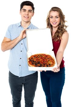 Young couple offering a medium sized delicious pizza to you.