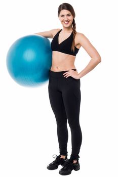 Fit gym woman striking a pose with an exercise ball against her waist.