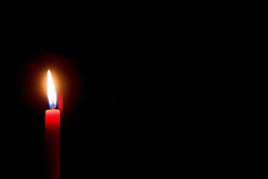 burning red candle with black background and space for text