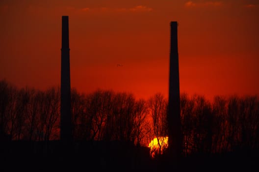 Silhuette of two chimneys in front of a red sunset.