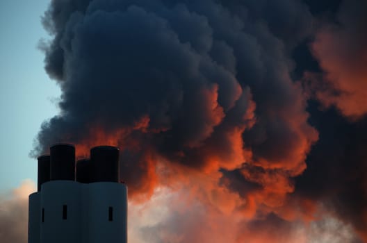 Pollution concept of smoking chimney. The setting sun illuminates the vapor from below, giving it an ominous impression, like that of volcano smoke.