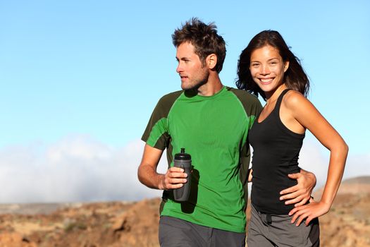 Young multicultural couple outdoors in sporty outfit. Portrait after running workout outside in mountains. Asian sport fitness woman and Caucasian man models.