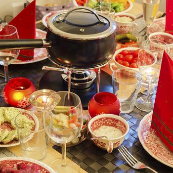 A well-laid table with a fondue caquelon, vegatables and dishes. Square format.