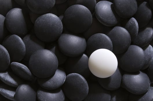 A white go stone on a pile of black stones. Go is a traditional Chinese strategic board game. It is considered to be one of the oldest games in the world.