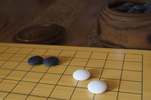 A set of the traditional Asian board game go. A bowl with black stones is in the background. Shallow depth of field.