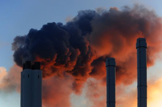 Pollution concept of smoking chimneys. The setting sun illuminates the vapor from below, giving it an ominous impression, like that of volcano smoke.